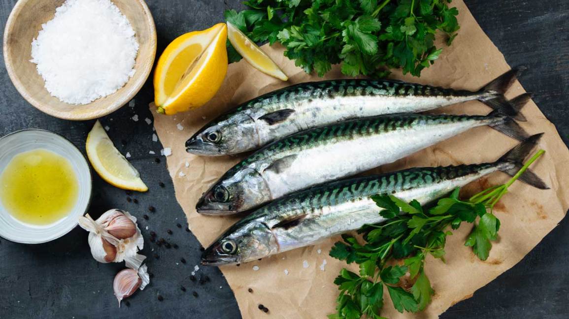 Three mackerel on a wooden serving platter with lemon and herbs.